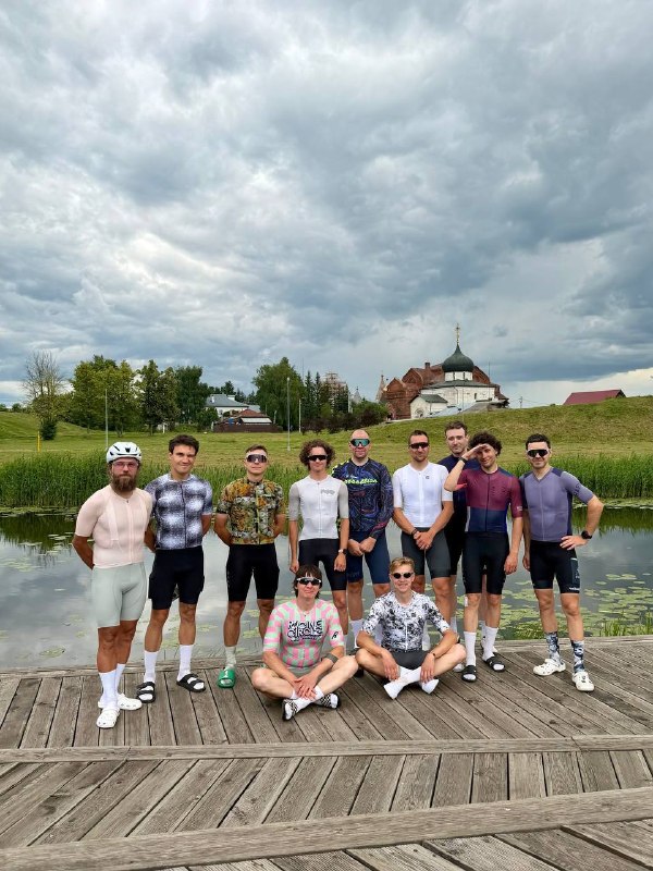 Двенадцать участников заезда Midsummer 300+ стоят вместе на деревянном пирсе у воды